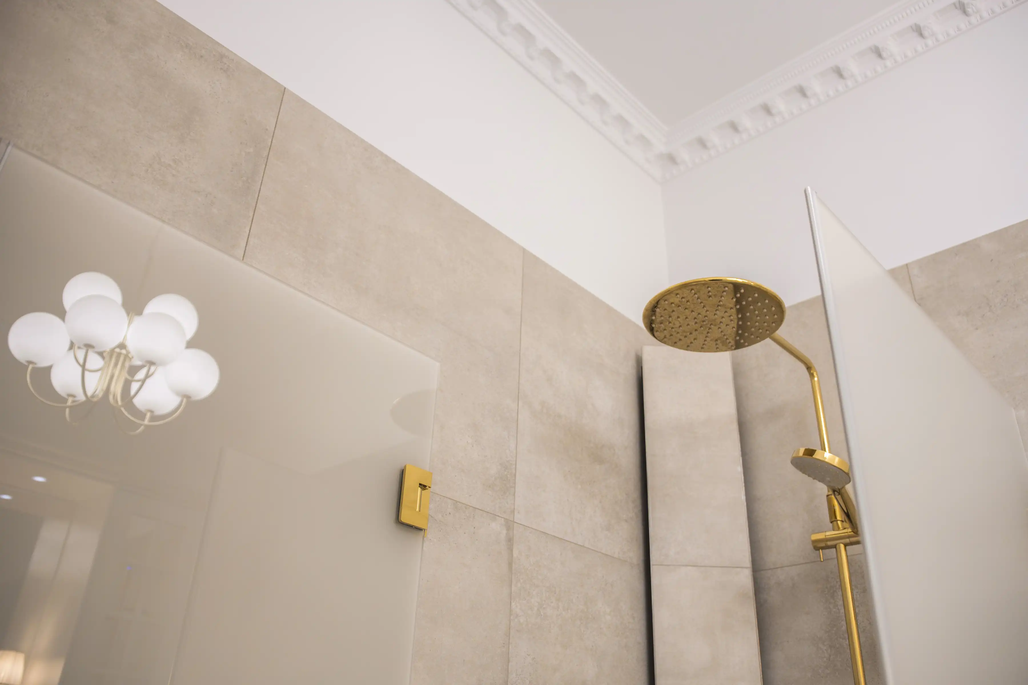 Badrum med stuckatur i tak, mässingsdusch och beige kakel i sekelskiftesstil