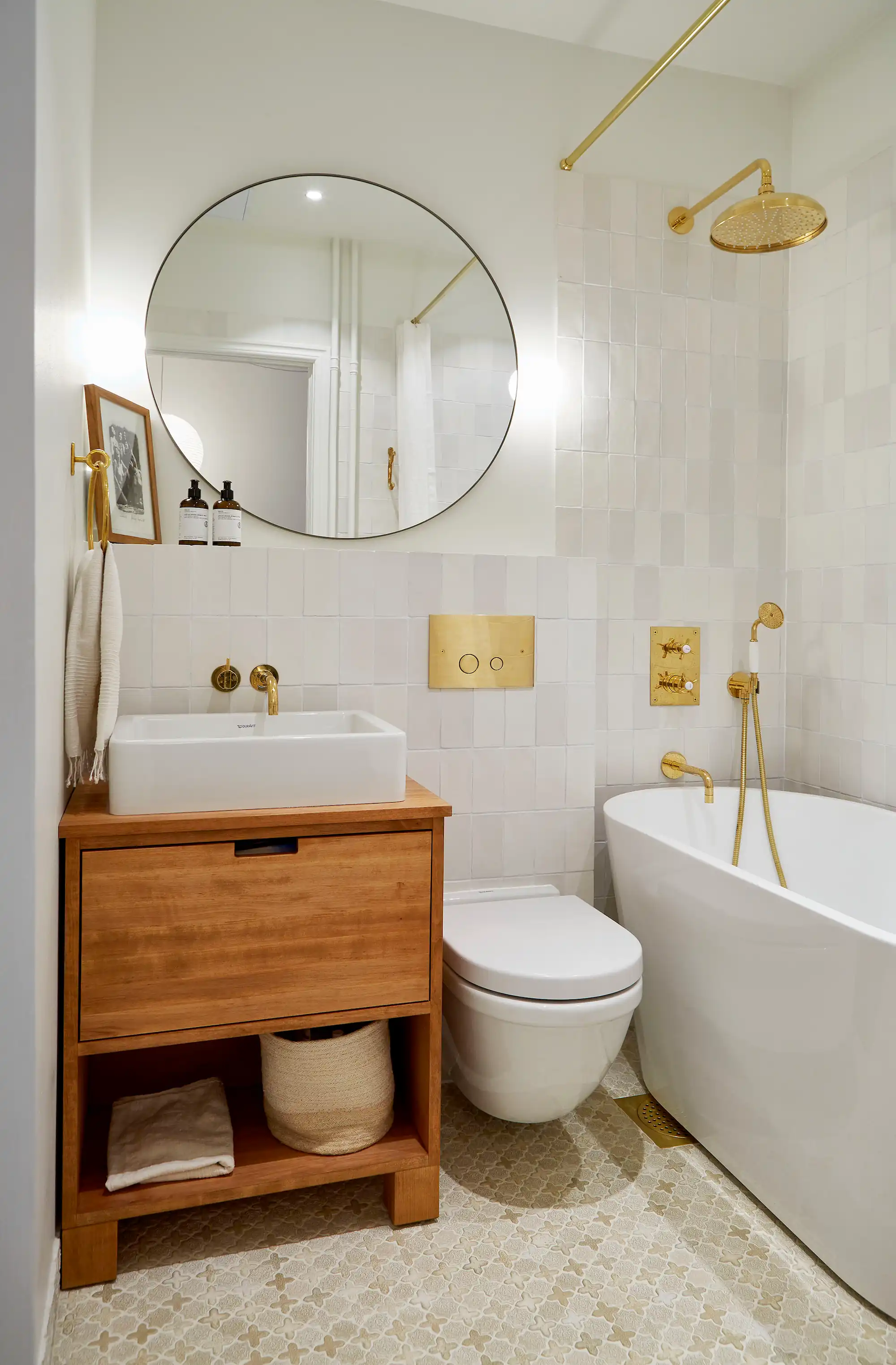 badrumsrenovering efter-bild med ljust kakel, badkar,kommod i trä och mässingsdetaljer