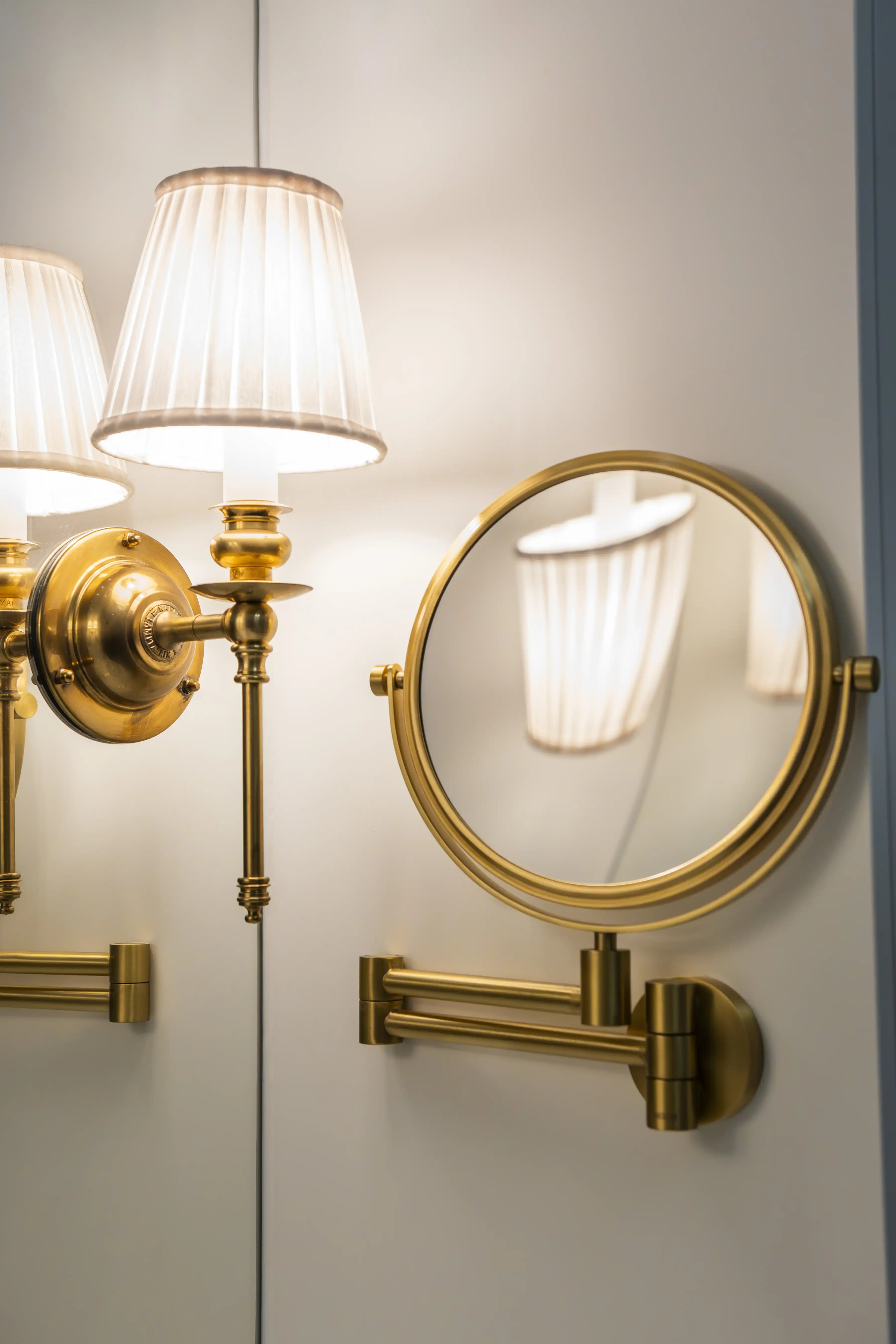 närbild på sminkspegel och vägglampa  i mässing med vit bakgrund